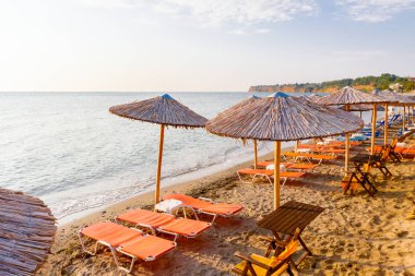 Sabahın erken saatlerinde güneş, şafak, halk plajında sazlı güneş gözlükleri, şemsiyeler ve deniz kıyısı boyunca iskemlelerle.