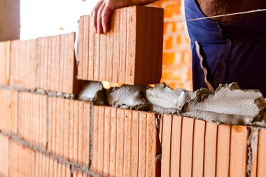 Mason, tuğla ustası düz olması için tel hattının yanına duvar örüyor..