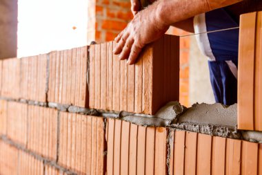 Mason, tuğla ustası düz olması için tel hattının yanına duvar örüyor..