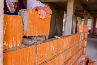 Mason, çimento çalışan inşaat sahasında bir duvara monte için kırmızı blokları kullanıyor.