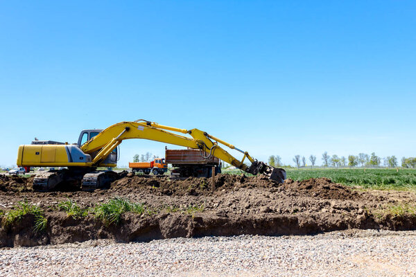 Большой экскаватор засыпает самосвал грунтом на строительной площадке, проект находится в стадии разработки.