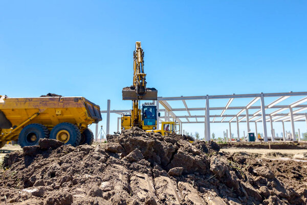 Big excavator is filling a dumper truck with soil at construction site, project in progress.