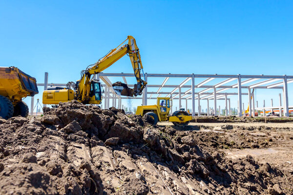 Big excavator is filling a dumper truck with soil at construction site, project in progress.