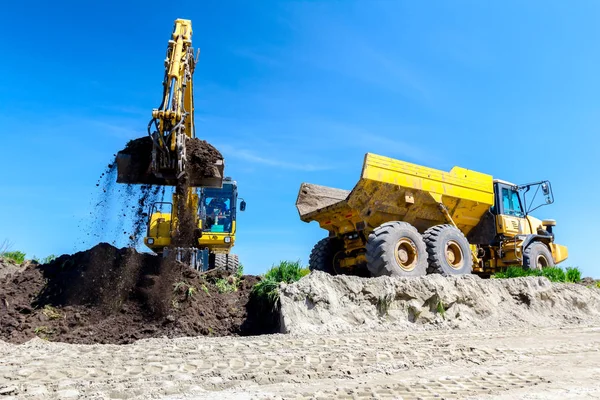 大きな掘削機は建設現場で土壌でダンパートラックを充填しています 進行中のプロジェクト — ストック写真