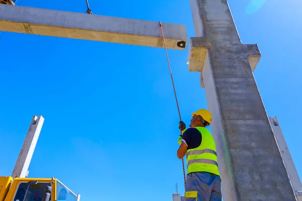 Worker is helping mobile crane with rope to manage concrete joist for assembly huge construction.