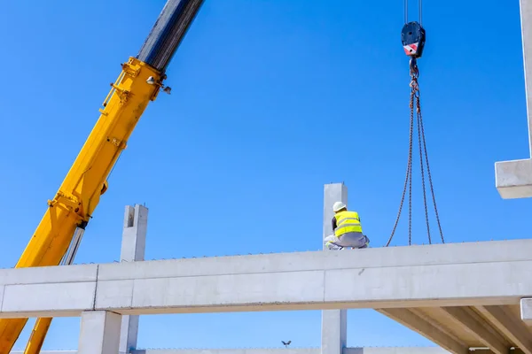 労働者はアセンブリの巨大な建設のためのコンクリートの梁を管理する移動式クレーンを支援します — ストック写真