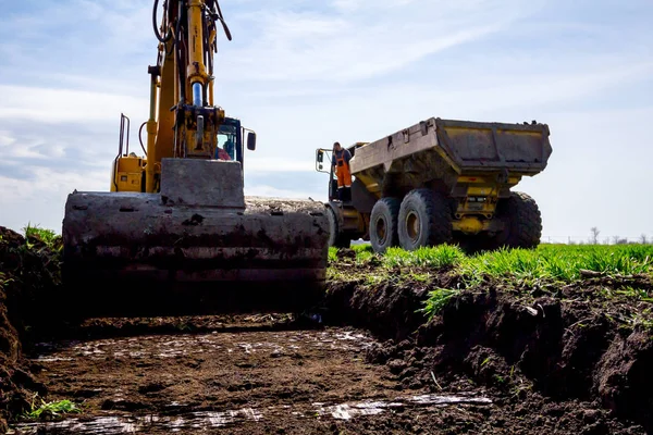 Excavatrice charge un camion avec le sol sur le chantier de construction — Photo