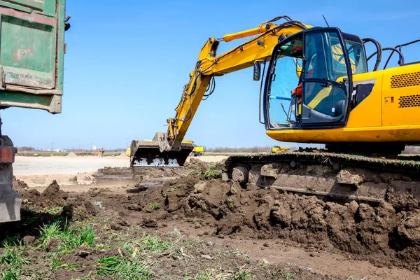 Excavadora está cargando un camión con tierra en el sitio de construcción — Foto de Stock