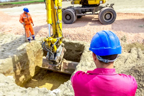 Chefe supervisiona, controlando escavadeira até que está cavando em buildin — Fotografia de Stock