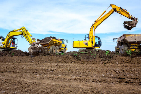 Big excavators are loading two trucks with ground on building si