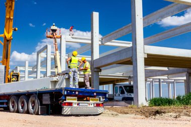İşçi kamyon yolundaki beton kirişe vinç kancaları takıyor.