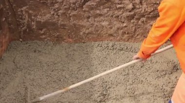 İşçiler beton dökerek temizliyor. Mason, hendeğe taze beton serpmek için tırmık kullanıyor..