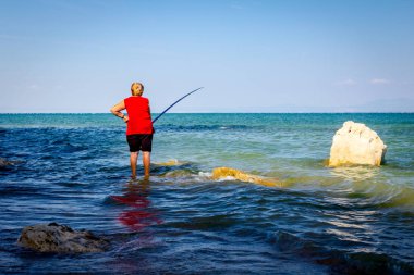 Yaşlı kadın sığ denizde balık tutuyor.