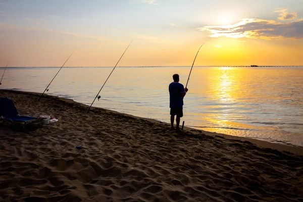 Silhouette eines Mannes, der morgens am Strand fischt — Stockfoto