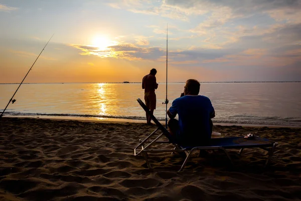 Silhouette von zwei Freunden, die in der Sonne am Strand fischen — Stockfoto