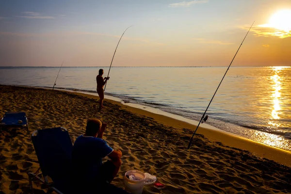 Silhouette von zwei Freunden, die in der Sonne am Strand fischen — Stockfoto