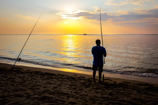 Silhouette of man who is fishing on the beach in sunrise morning Stock Photo