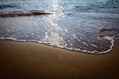 Deniz kumlu plajda köpüklü dalgalar kırıyor, sahil