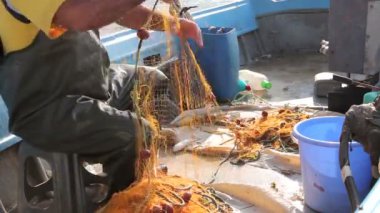 Fisher kauçuk pantolon ve çizme onun tekne de oturarak ve açık denizde olta için balıkçılık ağı kazık. Fotoğraf - Jpeg video codec