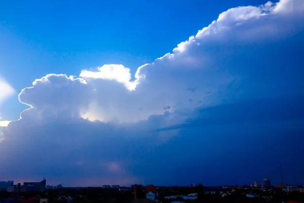 Mavi bir gökyüzünde bulutlardan güneş ışığı ışınları, distanc şehir — Stok fotoğraf