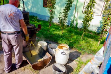 Adam, kullanılmış meyve suyu, brendi, konyak, viski, viski, cin ve viski gibi alkollü içecekler yapmak için bakırdan yapılmış ev yapımı içki imalathanesini boşaltıyor..