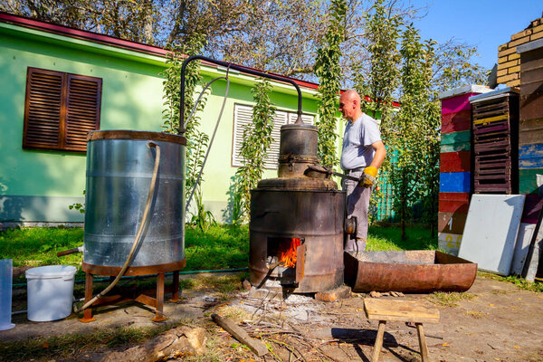 Человек вручную поворачивает рычаг, чтобы смешать фруктовый марк в котле самодельного ликеро-водочного завода из меди, делая самогон шнапс, алкогольные напитки, такие как бренди, коньяк, виски, бурбон, джин, скотч.
