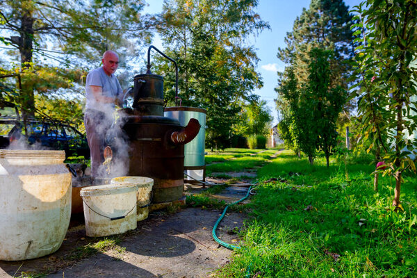 Человек разгружает котел самодельного ликеро-водочного завода из меди для выпуска подержанных фруктов марки, делая самогон шнапс, алкогольные напитки, такие как бренди, коньяк, виски, бурбон, джин и скотч.