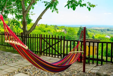 Multi colored hammock made from strong fabric is hanging on ropes view on hilly landscape. clipart