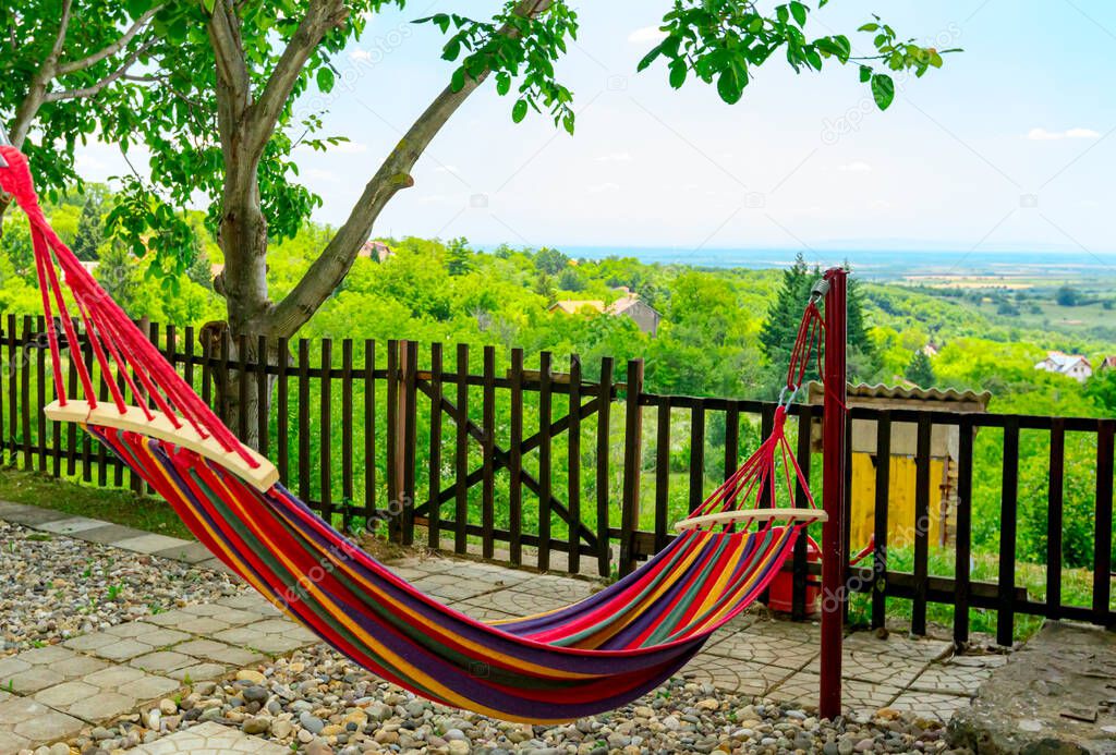 Multi colored hammock made from strong fabric is hanging on ropes view on hilly landscape.