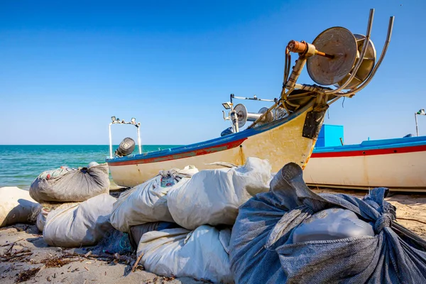 Heap of commercial fishing net placed on the beach and extraction mechanism on the boats.