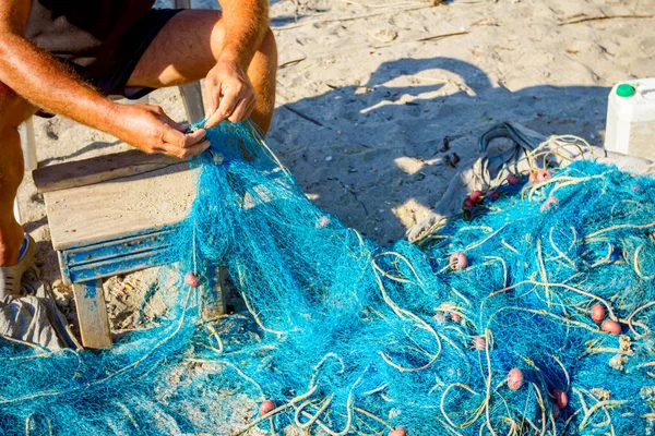 一位渔夫坐在海滩上的椅子上 把渔网堆积起来 从贝壳中清理干净 — 图库照片