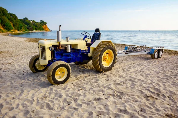 Tractor with empty trailer is parked on the sandy beach, waiting for transport boats.