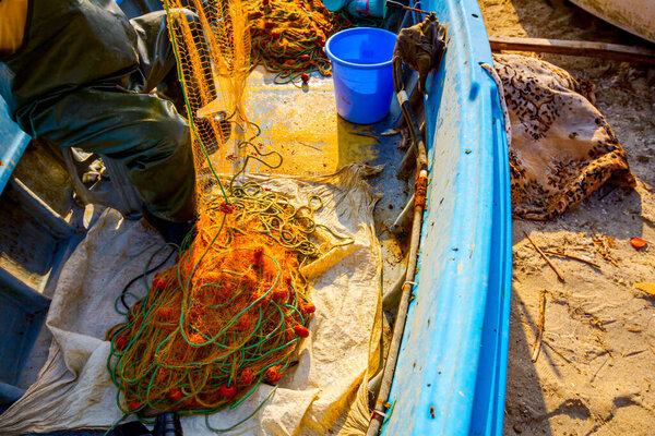 Fisher in rubber trousers and boot is sitting in his boat and pile up fishing net for angling at open sea.