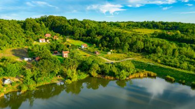 Toprak setin üstünde, tepe arazisindeki göl barajı, orman arazisi, kır yolu ve kır evi yerleşimi..