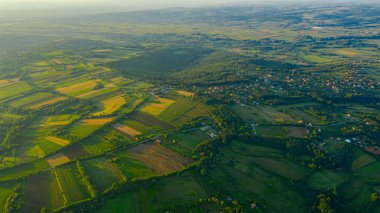 Yeşil tepe manzarasının üzerinde çekilmiş, uzaktaki orman ağaçları ve şehirler arasında ekilmiş araziler..