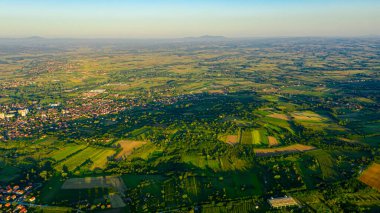Yeşil tepe manzarasının üzerinde çekilmiş, uzaktaki orman ağaçları ve şehirler arasında ekilmiş araziler..
