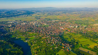 Yeşil tepenin üzerinde gölle çekilmiş, uzaktaki orman ağaçları ve şehirler arasında ekilmiş araziler..