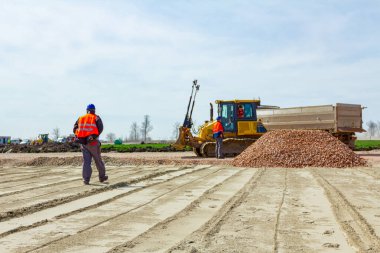 İnşaat işçisi, yönetici, güvenlik yeleği ve miğferli çalışanlara talimat veriyor buldozer ve kamyon şoförü kesirleri boşalttıktan sonra, kamyon römorkundan küçük parçalanmış taş.