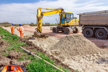 İşçiler, inşaat alanındaki hendek kazısını bitirmek için kazıcıyı bekliyor..