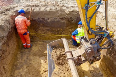 İşçiler, metrekarelik siperlerdeki ölçümleri kontrol etmek için metal mezura ve metre kullanıyorlar..