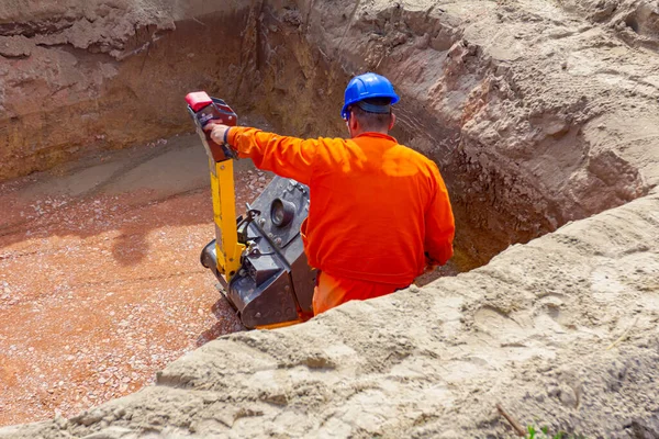 Worker is compacting gravel with vibration plate compactor machine in square trench.