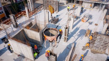 İnşaat işçilerinin üzerinde konik metal kova boşaltma, taşıma ve yüksek beton karışımı taşıma, binanın sütunları için uzun dikey kalıp beton dökümü olarak, koni tankı taşırken vinç kullanın.