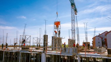 Kule vinci üzerinde koni tankı, beton karışımını taşımak ve taşımak için konik metal kova, inşaat sahasının üzerine dökülmek için, yeni tamamlanmamış çok katlı bina.