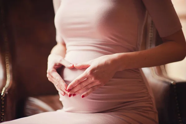 Hamile mutlu kadın karnına dokunuyor. Hamile orta yaşlı anne portresi, karnını okşayıp yakın çekimde gülümsüyor. Sağlıklı Gebelik kavramı, mavi arka plan üzerinde esmer beklentisi kadın