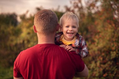Baba küçük oğlunu dışarıda sırtında taşıyor.