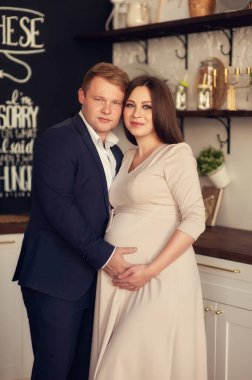 Yakışıklı adam güzel hamile karısının karnını dinliyor ve gülümsüyor.