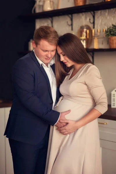 Yakışıklı adam güzel hamile karısının karnını dinliyor ve gülümsüyor.