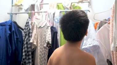 Geri giysiler arayan bir çocuk evde, yaşam kavramı asılı.