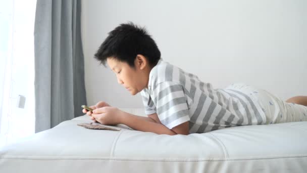 ベッドの上に横たわると自宅のラップトップを使用してアジアのプレティーンの少年 — ストック動画