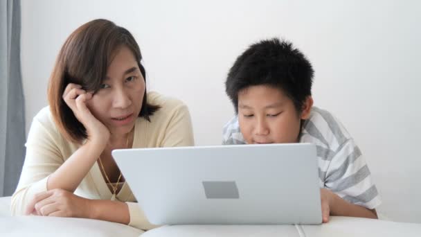11岁的男孩躺在床上和他的母亲玩笔记本电脑 — 图库视频影像
